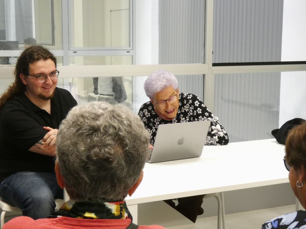 Membre de Versedia souriant tandis qu'une personne âgée heureuse lit une anecdote de sa biographie.